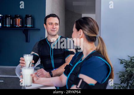 Jeune homme et femme souriants en costumes ems communiquent et boivent des shakes protéinés dans un bar sportif. Banque D'Images