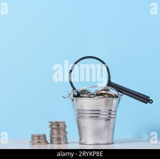 Une pile de pièces de monnaie en métal et une loupe en plastique sur fond bleu. Le concept de l'augmentation des impôts, des subventions Banque D'Images