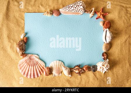 Maquette d'invitation ou de carte de voeux dans le cadre de coquillages et d'étoiles de mer sur le fond de plage de sable de l'océan. Banque D'Images