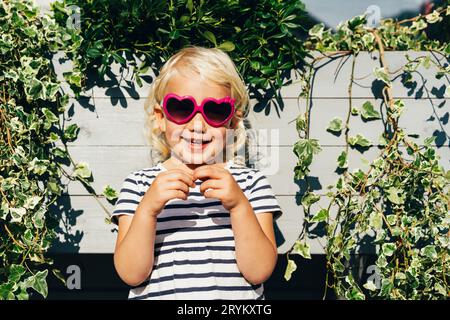 Petite fille blonde riante heureuse dans les lunettes de soleil regarde la caméra. Ambiance estivale Banque D'Images