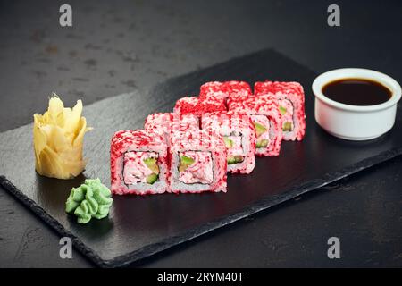 Rouleaux de sushi avec caviar de poisson volant tobiko rose vif, concombre et crabe sur fond sombre. Menu sushi. Cuisine japonaise. Banque D'Images