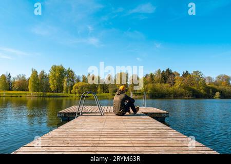 Jeune homme assis seul sur un pont en bois et regardant le lac Banque D'Images