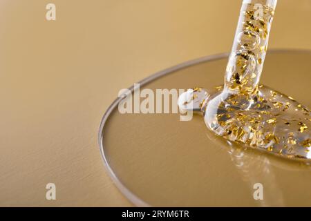 Pipetez et gels de produits cosmétiques dorés dans une boîte de Pétri sur fond beige Banque D'Images