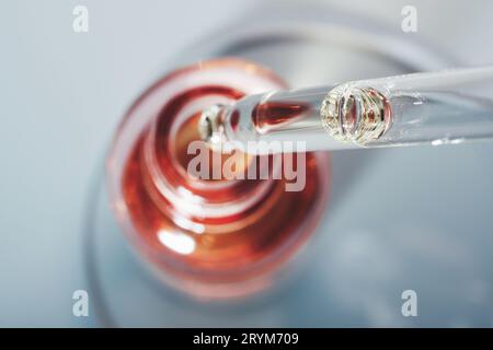 Bouteille d'huile ou de sérum et pipette dans une boîte de Petri sur fond gris. Produit cosmétique rose, concentration sélective Banque D'Images