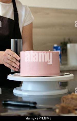 Femme chef pâtissier faisant un gâteau au chocolat avec de la crème rose, gros plan. Processus de fabrication de gâteau, focalisation sélective Banque D'Images