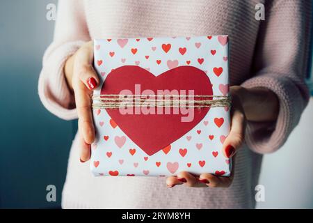 Gros plan d'une boîte cadeau décorée d'un coeur rouge dans les mains d'une femme méconnaissable. Banque D'Images