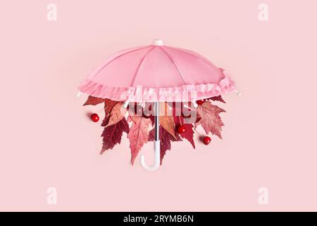 Les feuilles d'automne tombent du parapluie rose sur fond pastel rose. Concept créatif Hello Autumn Banque D'Images