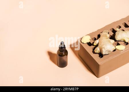 Huile essentielle de gingembre biologique en bouteille en verre foncé, racine de gingembre et brique sur fond beige. Vue isométrique, espace de copie Banque D'Images