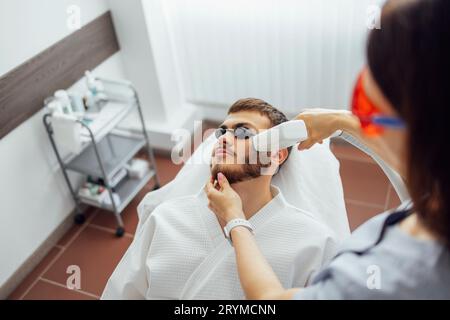 Jeune homme recevant l'épilation photo tout en visitant le centre de beauté sur le salon Banque D'Images