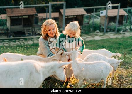 Une maman et une petite fille souriantes se nourrissent et s'occupent des chèvres à la ferme.L'agritourisme à la campagne. Banque D'Images