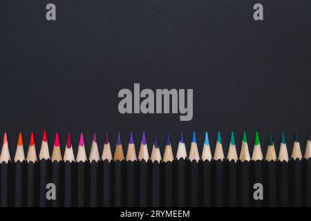 Fond de papeterie minimal.jeu de crayons de couleur disposés en ligne sur fond noir Banque D'Images