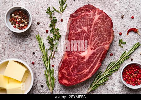 Steak d'oeil de côte de bœuf marbré frais, beurre et épices sur fond de pierre grise, gros plan Banque D'Images