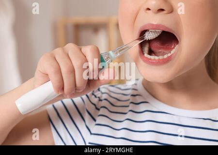 Petite fille se brossant les dents avec une brosse à dents électrique à l'intérieur, gros plan Banque D'Images