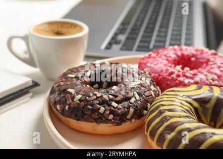 Mauvaises habitudes alimentaires sur le lieu de travail. Beignets glacés sucrés sur table blanche, gros plan Banque D'Images