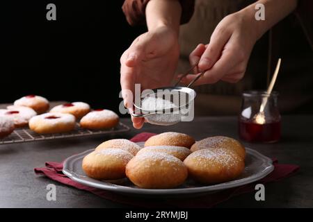 Femme saupoudrant le sucre en poudre sur de délicieux beignets Hanukkah sur la table grise, gros plan Banque D'Images