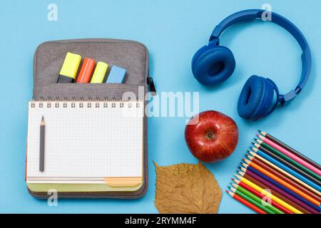 Crayons de couleur, une pomme, un casque, livre d'exercices ouvert sur le sac à crayons Banque D'Images