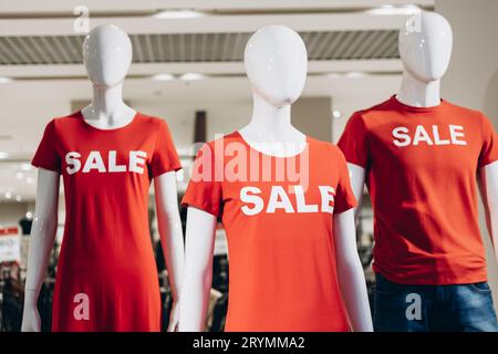 Les mannequins de mode en T-shirts rouges et les SMS vendus sont placés dans la vitrine du magasin et attirent les acheteurs. Solde du Vendredi fou dans un magasin décontracté Banque D'Images