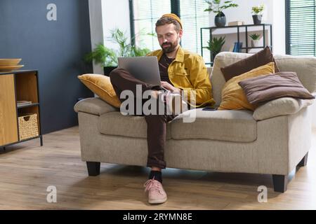 Homme assis à la maison, absorbé dans l'ordinateur portable, tape des commentaires dans les réseaux sociaux sur Internet. Homme avec un demeano unique et excentrique Banque D'Images