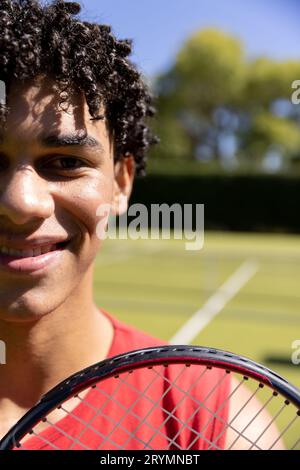 Demi portrait d'homme biracial à la bonne tenue avec raquette de tennis sur un court de tennis extérieur ensoleillé, espace copie Banque D'Images