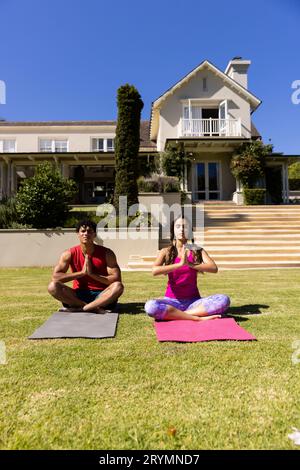 Joyeux couple de forme diverse pratiquant la méditation de yoga assis dans le jardin ensoleillé, avec l'espace de copie Banque D'Images
