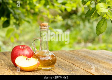 Vinaigre de pomme dans la bouteille en verre et pommes rouges fraîches sur les planches de bois Banque D'Images