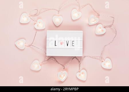 Plat minimal Valentine avec mot amour sur un tableau lumineux et guirlande en forme de cœur. Décoration Saint-Valentin Banque D'Images