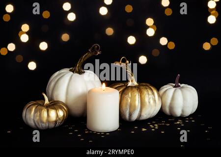 Composition festive Halloween ou Thanksgiving Day avec citrouilles dorées et bougie allumée sur fond noir. Vue avant Banque D'Images