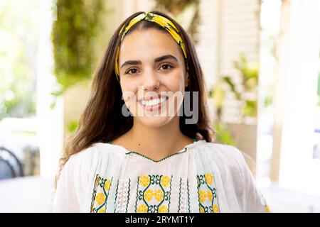 Portrait d'une jeune femme biraciale portant un bandeau jaune assis à la maison, espace de copie Banque D'Images