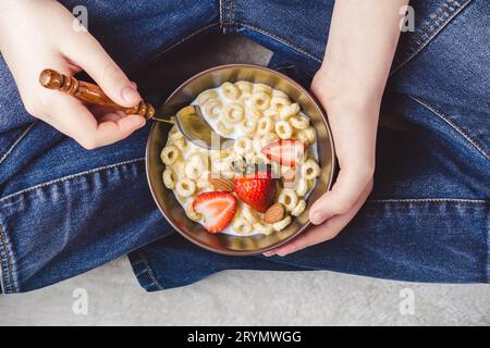 Bol de petit déjeuner traditionnel. Anneaux de céréales, fraises et amandes avec du lait dans un bol dans les mains des adolescents Banque D'Images