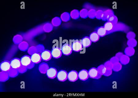 Les lumières de bokeh néon violettes bouclent sur le noir. Fond abstrait pour votre conception Banque D'Images