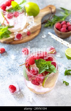 Cocktail seltzer dur avec framboises et citron vert sur un plateau en pierre grise. Banque D'Images