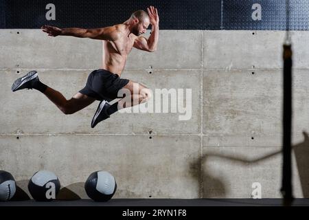 Un homme musclé capturé dans l'air alors qu'il saute dans une salle de gym moderne, mettant en valeur son athlétisme, sa puissance et sa détermination à travers un highi Banque D'Images