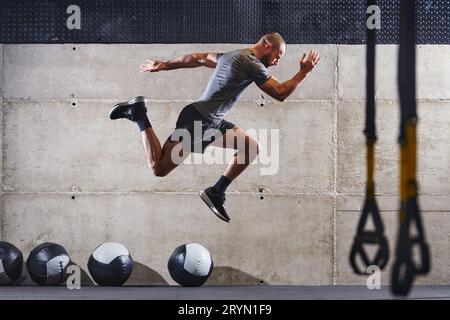 Un homme musclé capturé dans l'air alors qu'il saute dans une salle de gym moderne, mettant en valeur son athlétisme, sa puissance et sa détermination à travers un highi Banque D'Images