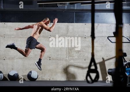 Un homme musclé capturé dans l'air alors qu'il saute dans une salle de gym moderne, mettant en valeur son athlétisme, sa puissance et sa détermination à travers un highi Banque D'Images