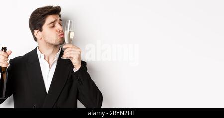 Gros plan d'un beau homme en costume, verre de baiser avec champagne, s'ivre lors d'une fête, debout sur fond blanc Banque D'Images