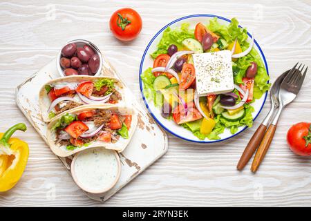 Cuisine grecque traditionnelle : salade grecque, Gyros avec viande et légumes, sauce Tzatziki, olives sur table blanche rustique en bois backgro Banque D'Images