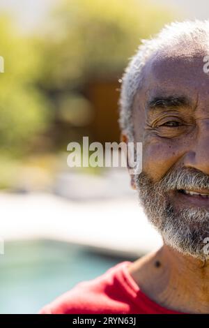 Demi portrait d'un homme biracial senior heureux avec une barbe souriante dans un jardin ensoleillé, espace copie Banque D'Images