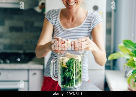 Une jeune femme place les ingrédients d'un smoothie dans un bol mélangeur. Concept de saine alimentation. Banque D'Images