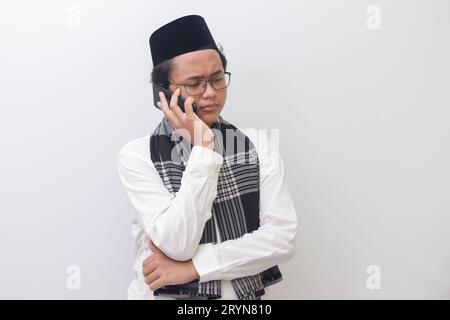 Portrait d'un jeune homme musulman asiatique faisant un appel téléphonique. Image isolée sur fond blanc Banque D'Images