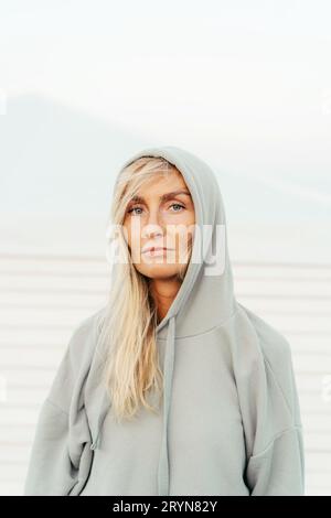 Femme blonde bronzée blanche de trente ans dehors dans un sweat à capuche gris. Portrait vertical monochrome en gros plan d'une femme avec un Scand Banque D'Images