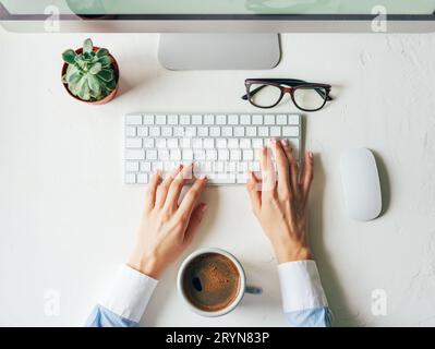 Vue de dessus sur les mains de travail sur un clavier d'ordinateur. Espace de travail lumineux. Minimalisme. Succulent et une tasse avec café fort Banque D'Images