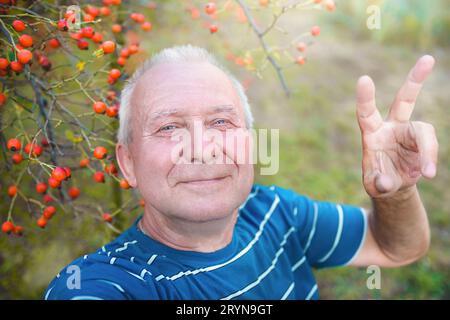 Grand-père retraité positif, fait selfie photo avec un smartphone dans le parc. un homme âgé marche dans la nature. Banque D'Images