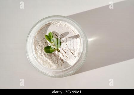 Un pot ouvert de poudre de gommage pour le visage avec une branche verte. Banque D'Images