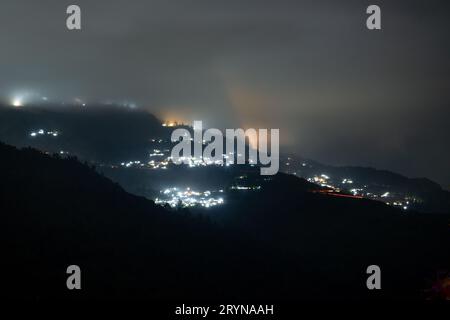 Photo de nuit montrant le village de darjeeling niché au milieu des montagnes de l'himalaya avec des lumières orange et bleues Banque D'Images