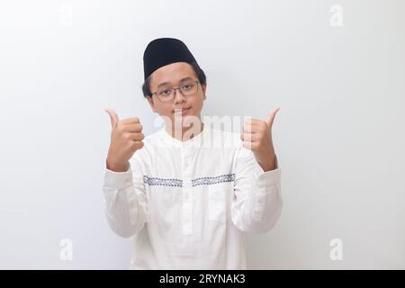 Portrait d'un jeune homme musulman asiatique souriant et regardant la caméra, faisant des pouces vers le haut geste de la main. Image isolée sur fond blanc Banque D'Images