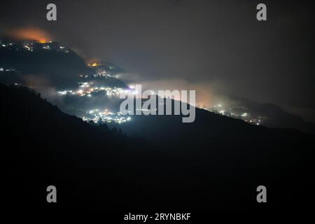 Photo de nuit montrant le village de darjeeling niché au milieu des montagnes de l'himalaya avec une lumière orange et bleue Banque D'Images