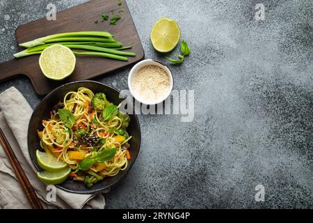 Nouilles végétariennes asiatiques avec des légumes et du citron vert dans un bol en céramique rustique noir, baguettes en bois, planche à découper avec gr haché Banque D'Images