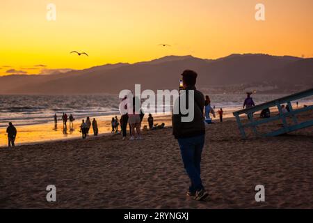 Homme prenant une photo du coucher de soleil sur la plage Banque D'Images