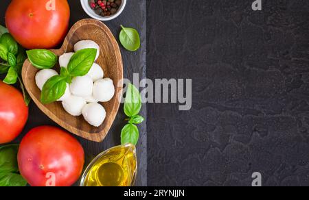 Fromage mozzarella, tomates et basilic sur une table en pierre noire. À Banque D'Images