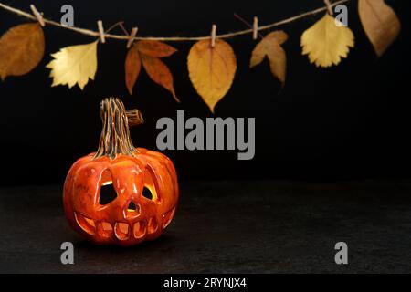 Lanterne de citrouille en céramique d'Halloween et guirlande de feuilles d'automne sur fond noir. Carte de vœux Banque D'Images